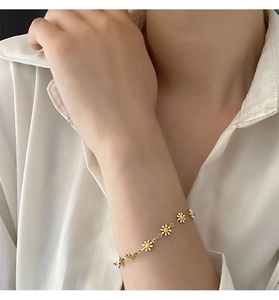 Detailed shot of a dainty golden daisy flower bracelet on a model wearing white linen