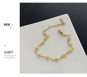 Detail of white daisy enamel bracelet with golden chain and lobster clasp on white platform