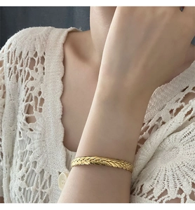 Close-up of golden braided wheat pattern metal bracelet worn on wrist with lace sleeve