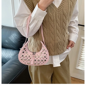 Detail of pink crescent bag with silver rivets shown on a model in a cozy indoor setting