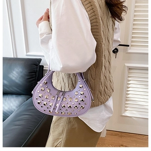Close-up of a lilac crescent leather shoulder bag with silver rivet studs on a model