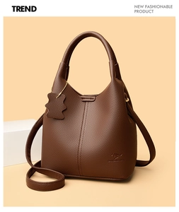 Détail d'un sac cabas en cuir marron foncé à motif litchi avec un pendentif d'ours