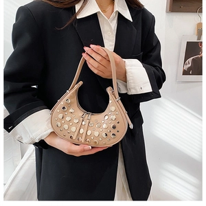 Detail view of crescent shoulder bag featuring silver rivets and beige faux leather