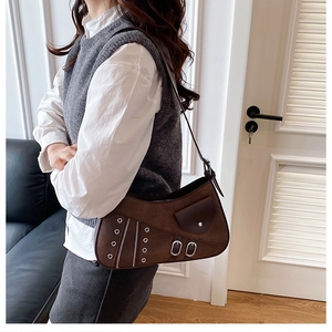 Detail of dark brown suede saddle bag with metal rivets and shoulder strap on model