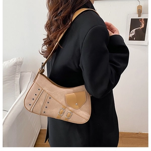 Detail view of beige suede saddle bag with metal eyelets and decorative zippers