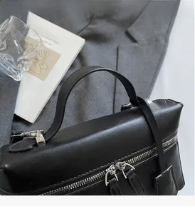 Detail of sturdy top handle and silver zipper on black matte leather crossbody bag