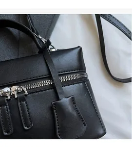 Détail d'un sac à main carré en cuir noir avec zips argentés et coutures précises