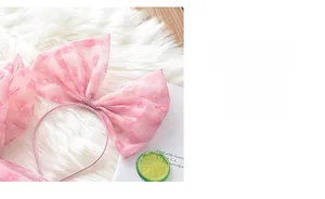 Détail d'un serre-tête rose à nœud avec motifs cœurs sur fond en fausse fourrure blanche