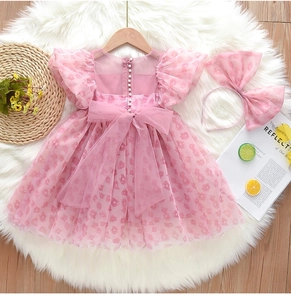 Détail de robe en tulle rose pour fille avec boutons perlés et grand nœud en résille