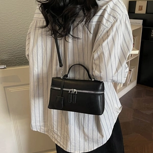 Détail d'un sac carré en cuir mat noir avec double fermeture éclair argentée et pendentif