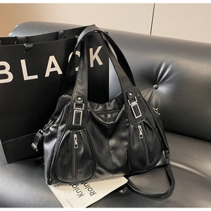 Detail of black faux leather tote bag with silver zippers on a black sofa setting