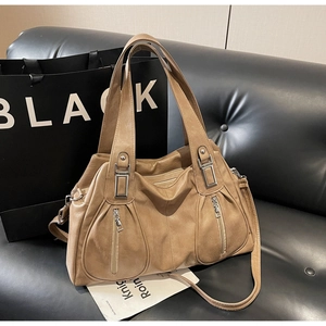 Close-up of tan leather tote bag with dual zippers on a black sofa for commute