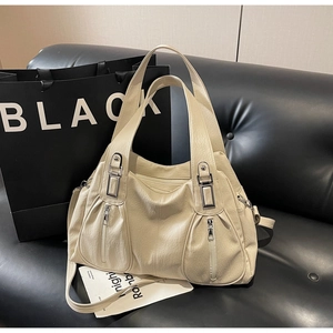 Detail of cream large tote bag with silver zippers and double handles on a black sofa