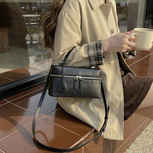 Détail d'un sac bandoulière noir porté avec un trench dans un décor de café urbain