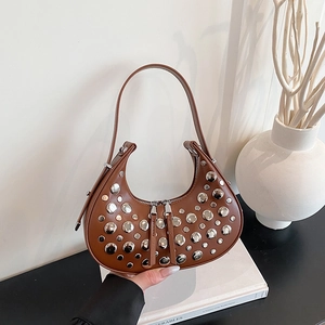 Brown half-moon underarm bag with silver rivets and vintage punk style on white books