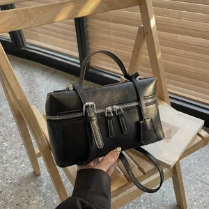 Détail d'un sac à bandoulière en cuir noir minimaliste avec fermetures éclair sur une chaise
