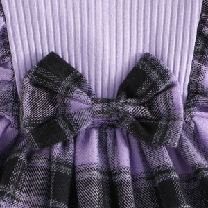 Detailed close-up of girls' knit dress with purple checkered patterns and bow accent