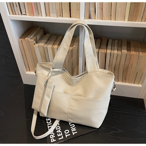 Detail view of large cream tote bag with cross stitching on a bookshelf backdrop