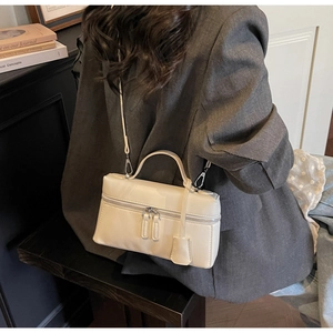 Détail d'un sac bandoulière blanc cassé en forme de boîte porté avec un manteau gris