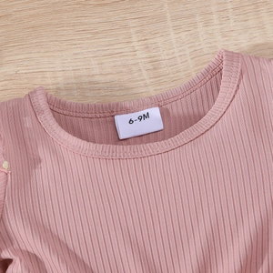 Close-up of pink ribbed fabric baby dress neckline with 6-9M size label on wood background