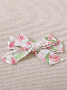 Close-up of baby floral bow headband with pink flowers on beige knit background