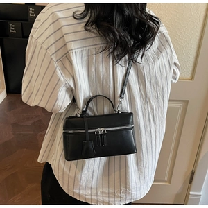 Détail d'un sac bandoulière noir en cuir avec double fermeture éclair et pendentif déco