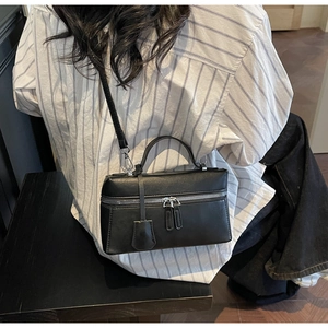Détail d'un sac à main carré noir avec fermetures éclair argentées et bandoulière fine