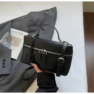 Détail d'un sac à main boîte noir avec double zip et accessoires argentés sur blazer