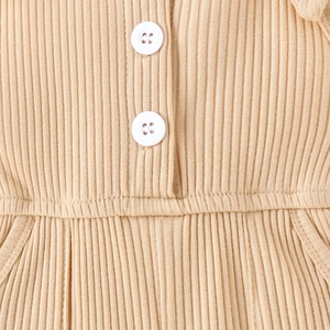 Dettaglio di maglia a coste beige con bottoni su una tuta intera da bambina