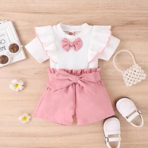 Detail von Baby-Mädchen-Set mit weißem Oberteil und rosa Shorts auf Holzboden