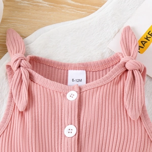 Dettaglio della tutina in maglia rosa con spalline a fiocco ed etichetta per neonata