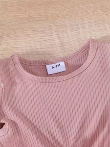 Close-up of pink ribbed cotton baby dress collar with size label on wooden background