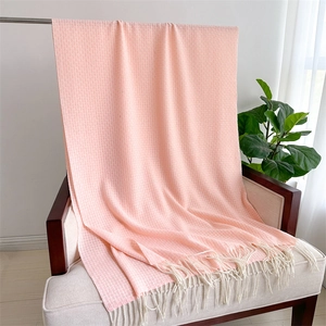 Détail d'une écharpe rose en maille gaufre avec franges blanches sur un fauteuil