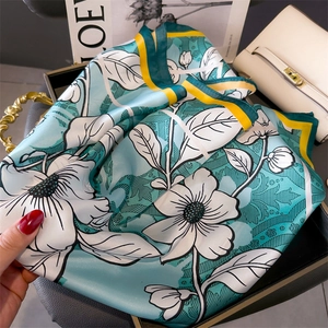 Detailed view of mint green floral silk scarf with geometric stripes on a stylish tray