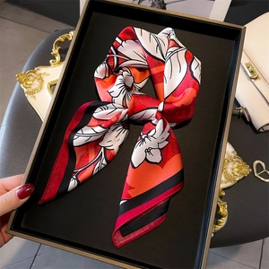 Close-up of a floral silk scarf bow with red and orange patterns on a black display tray