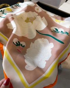 Détail d'un foulard en soie rose à fleurs avec bordure orange sur un sac en cuir