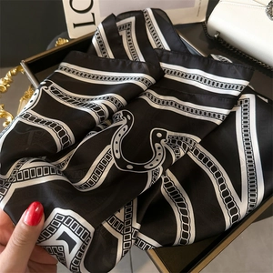 Detailed close-up of a black and white chain print silk scarf on a luxury tray
