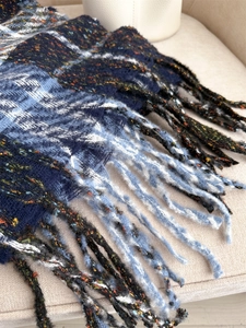 Close-up of thick plaid winter scarf featuring classic blue fringe and soft knit texture