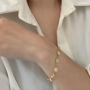 Delicate gold chain bracelet featuring white daisy flowers worn on a wrist over a shirt