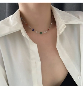 Close-up of a silver chain necklace with multi-colored heart pendants on model's neck