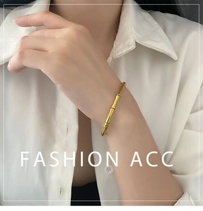 Gros plan d'un bracelet doré en forme de bambou porté sur une manche blanche