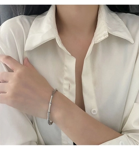 Détail d'un bracelet jonc argenté style bambou porté au poignet sur une chemise blanche