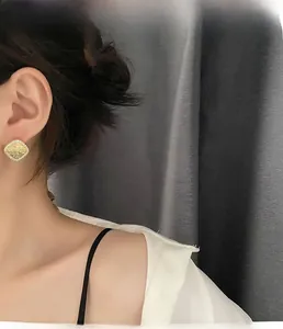 Detailed close-up of a square geometric gold stud earring worn on a model earlobe