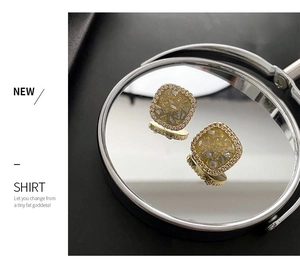 Detail of square gold crystal stud earrings with yellow resin stone on mirror