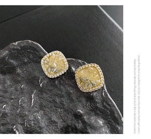 Close-up of square geometric stud earrings with yellow crystal and sparkling diamonds