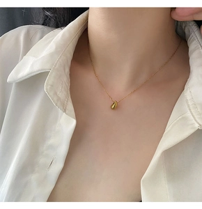 Close-up of a minimalist 18K gold teardrop pendant necklace worn on a white silk shirt