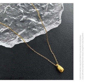 Macro view of gold teardrop pendant on a delicate chain against a dark textured background