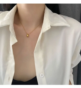 Close-up of a gold water drop pendant necklace on a delicate chain worn by a model