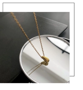 Close-up of golden teardrop pendant on minimalist chain with reflection in circular mirror