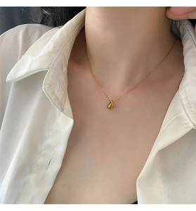 Close-up of a glossy gold teardrop pendant necklace worn over a white collared shirt